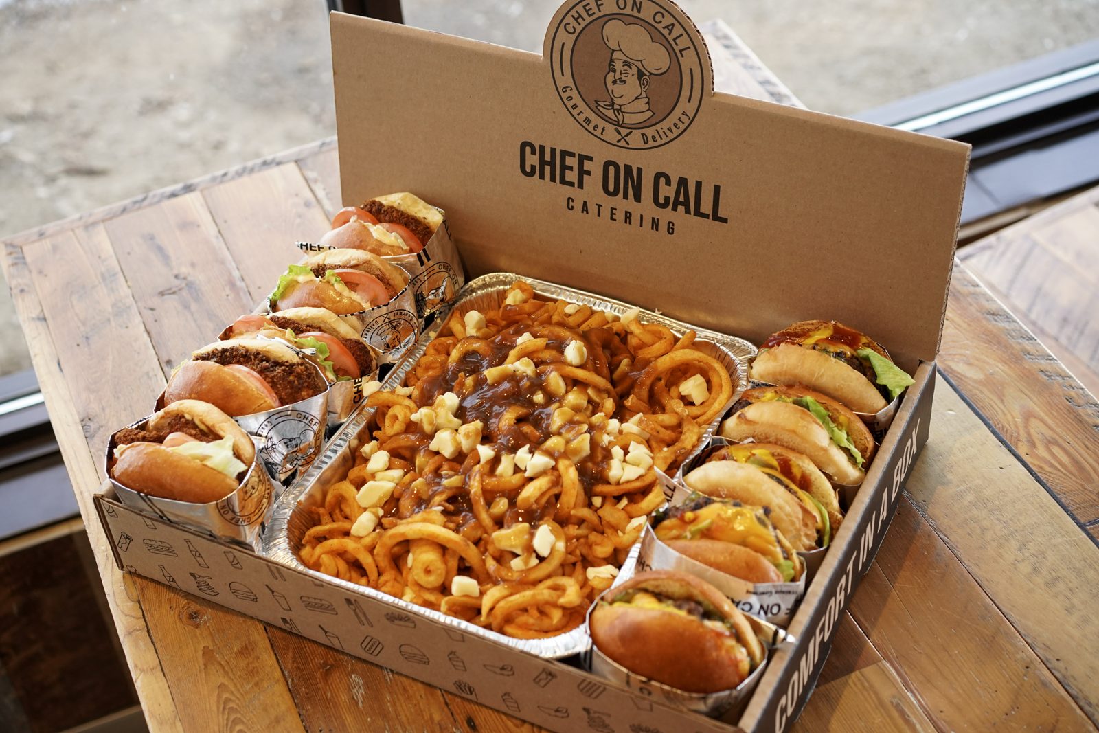 Open Chef On Call catering box with burgers around a curly fry poutine tray, ready for an office lunch