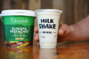 A person holds a milkshake cup of Chef on Call beside a container of milkshake, showcasing a delicious treat ready to enjoy.